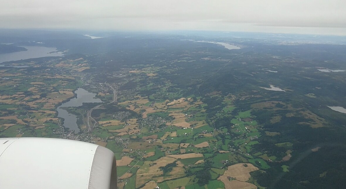the view from a plane, there's a fjord in the back and a lot of dark forrests