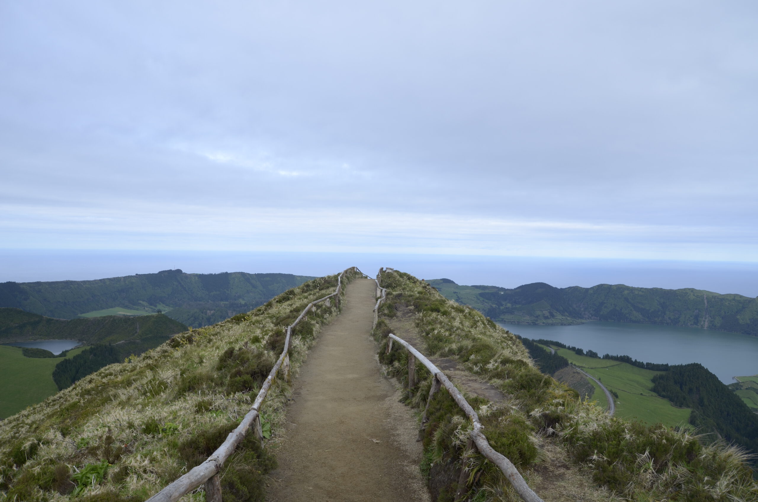 Das typische Azoren Postkartenmotiv: Ein Weg mit Holzgeländer der über einen Berg fühlt mit den Twin lakes am Hintergrund