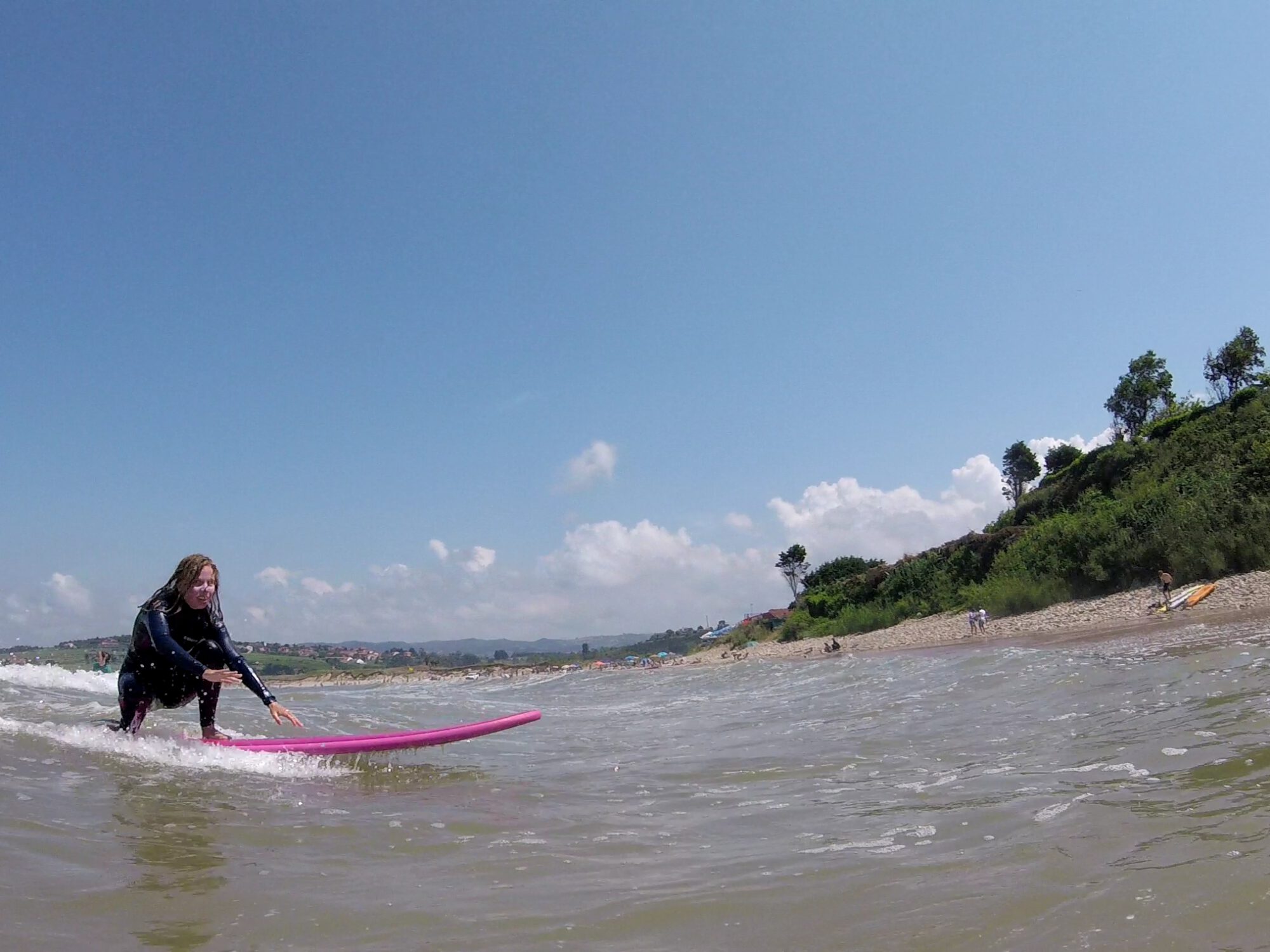 Eine Frau auf einem pinken Surfboard auf einer kleinen Welle...schon fast wieder am Strand