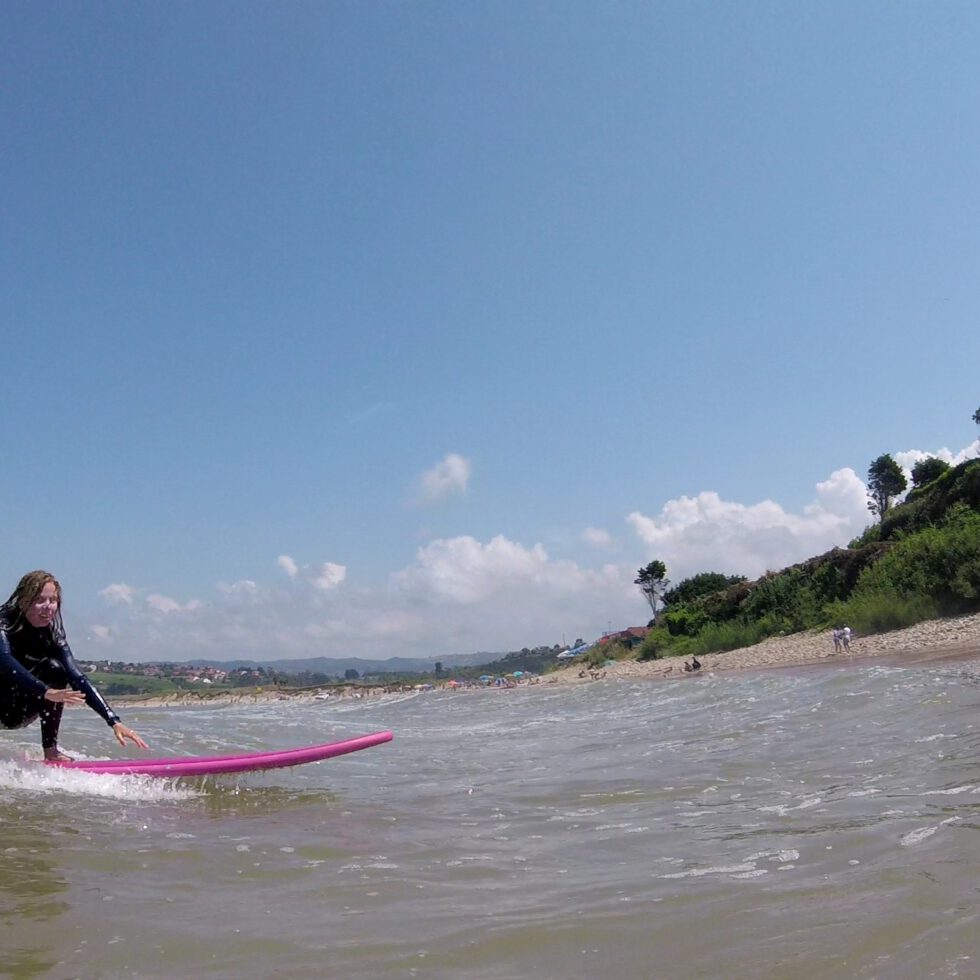Eine Frau auf einem pinken Surfboard auf einer kleinen Welle...schon fast wieder am Strand