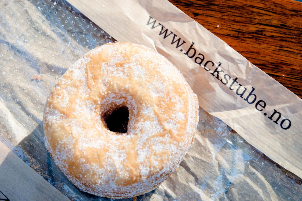 a round beige sugary donut made out of puff pastry, a cronut on a bag reading www.backstube.no