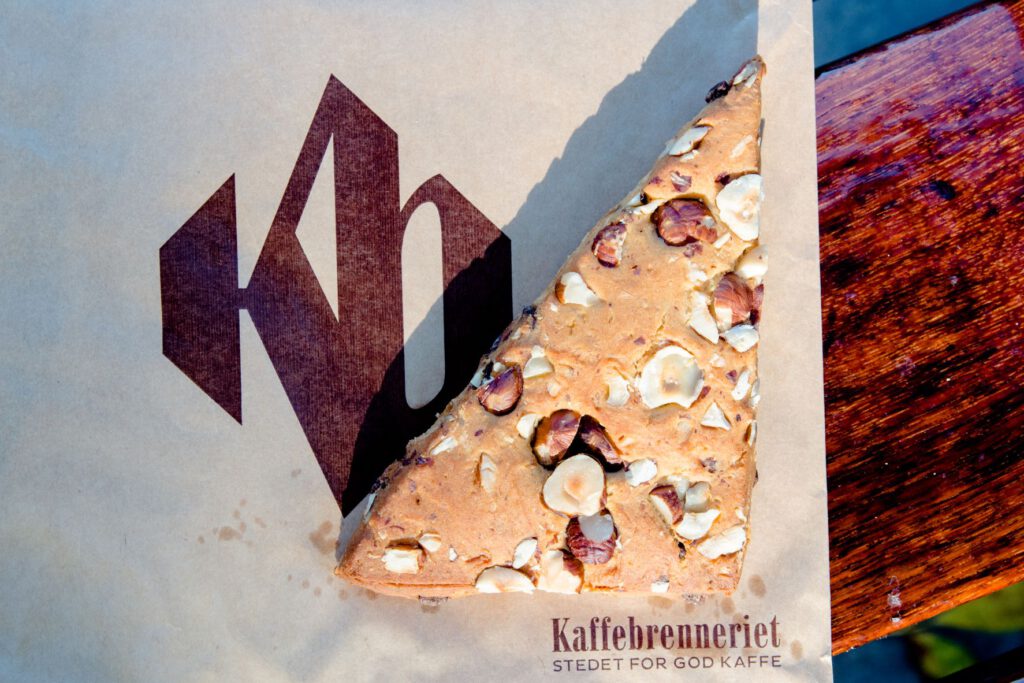 ein dreieckiges veganes Scone mit Haselnüssen und Schokolade liegt auf einer Papiertüte mit Aufdruck der Kaffebrenneriet